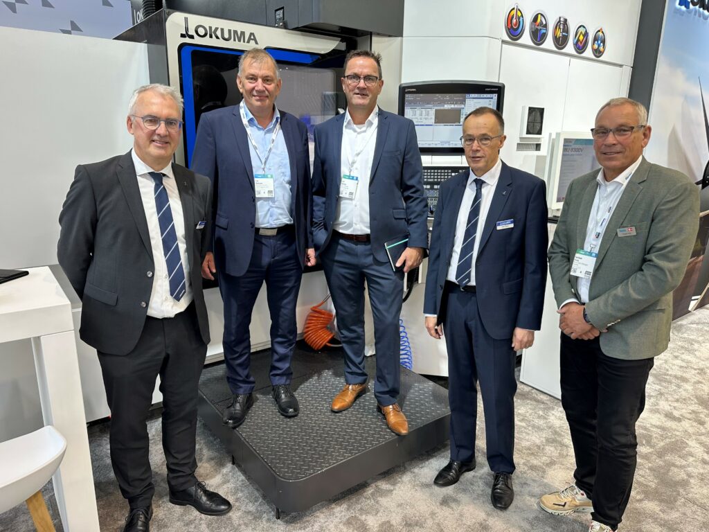 Fem repræsentanter fra LPM, RIVAL, Okuma og Flextek står foran en Okuma CNC-maskine på EMO-messen i Hannover.